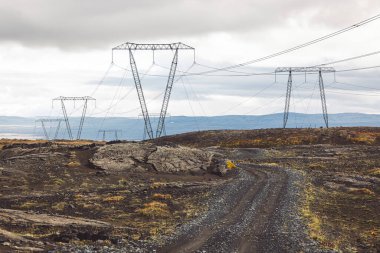 Yüksek voltajlı elektrik kabloları kutuplarda, bulutlu bir gökyüzünün arka planında. Çizgiler, cam yalıtımlarıyla kutuplara bağlanmış. Hatlar İzlanda 'nın dağlık bölgelerinden geçiyor. Yüksek kalite