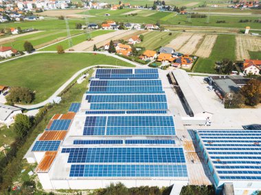 Güneş panelleri büyük bir endüstriyel binanın çatısına ya da bir depoya monte edilmiş. Slovenya 'nın kırsal kesimindeki sanayi binasında arka planda evler var. Yüksek kalite fotoğraf