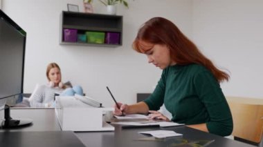 Yurt odasındaki oda arkadaşları, biri masanın başında bir proje üzerinde çalışırken, diğeri arka plandaki yatakta, dersten sonra dinleniyor.. 