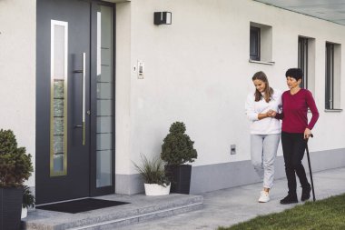 Genç, beyaz bir kadın, bir hemşire, yaşlı bir bayanla ilgilenen bir ev ziyaretinde. Hemşire, yaşlı bir kadına her gün ev işlerinde yardım ediyor. Yürümesine ve taşınmasına yardım ediyor.. 