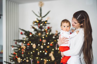 Genç anne ve kızının portresi, Noel 'de eğlenen küçük kız, Noel ağacını şenlikli kıyafetlerle süsleyen. Gülümseyen kız annesiyle oynuyor.. 