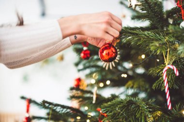 Noel ağacını süsleyen, ağaca kırmızı bir süs takan, elinde kırmızı bir Noel süsü tutan tanınmamış beyaz kadın.. 