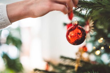 Noel ağacını süsleyen, ağaca kırmızı bir süs takan, elinde kırmızı bir Noel süsü tutan tanınmamış beyaz kadın.. 