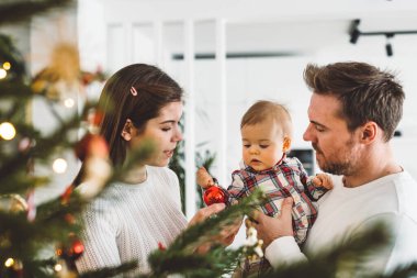 Üç çocuklu neşeli beyaz anne baba ve kız bebek Noel ağacını süslerken eğleniyorlar. Aile Noel portresi. 