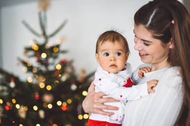 Genç anne ve kızının portresi, Noel 'de eğlenen küçük kız, Noel ağacını şenlikli kıyafetlerle süsleyen. Gülümseyen kız annesiyle oynuyor.. 