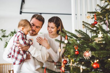 Üç çocuklu neşeli beyaz anne baba ve kız bebek Noel ağacını süslerken eğleniyorlar. Aile Noel portresi. 