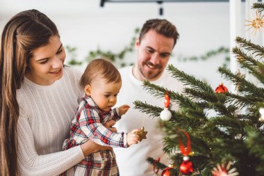 Üç çocuklu neşeli beyaz anne baba ve kız bebek Noel ağacını süslerken eğleniyorlar. Aile Noel portresi. 