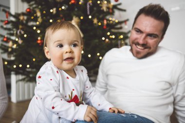 Baba ve kızı, Noel 'de eğlenen küçük kız, Noel ağacını şenlikli kıyafetlerle süsleyen. Gülümseyen kız babasıyla oynuyor.. 