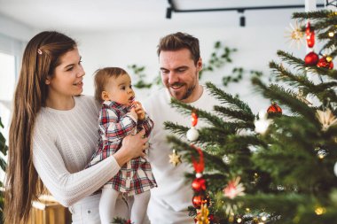Üç çocuklu neşeli beyaz anne baba ve kız bebek Noel ağacını süslerken eğleniyorlar. Aile Noel portresi. 