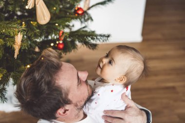 Baba ve kızı, Noel 'de eğlenen küçük kız, Noel ağacını şenlikli kıyafetlerle süsleyen. Gülümseyen kız babasıyla oynuyor.. 