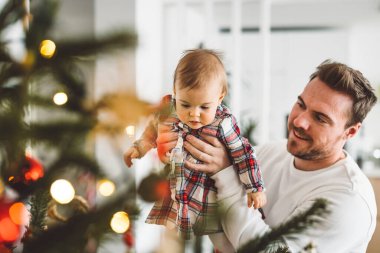 Baba ve kızı, Noel 'de eğlenen küçük kız, Noel ağacını şenlikli kıyafetlerle süsleyen. Gülümseyen kız babasıyla oynuyor.. 