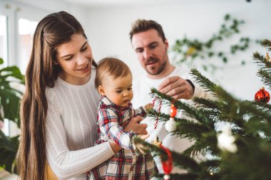 Üç çocuklu neşeli beyaz anne baba ve kız bebek Noel ağacını süslerken eğleniyorlar. Aile Noel portresi. 