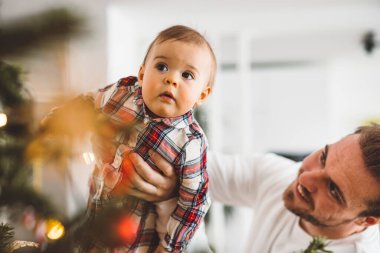 Baba ve kızı, Noel 'de eğlenen küçük kız, Noel ağacını şenlikli kıyafetlerle süsleyen. Gülümseyen kız babasıyla oynuyor.. 