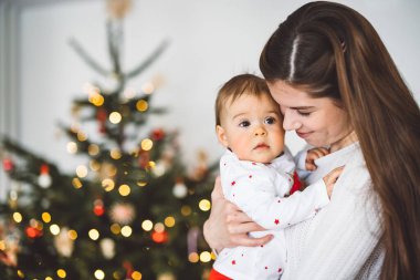 Genç anne ve kızının portresi, Noel 'de eğlenen küçük kız, Noel ağacını şenlikli kıyafetlerle süsleyen. Gülümseyen kız annesiyle oynuyor.. 