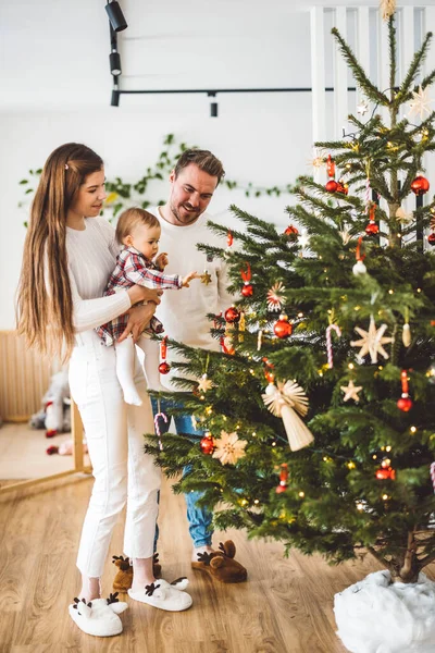 Üç çocuklu neşeli beyaz anne baba ve kız bebek Noel ağacını süslerken eğleniyorlar. Aile Noel portresi. 