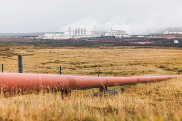 Geothermal Power Plant, hot water power station in Iceland. Steam rolling out of the plant chimneys, red large tubes running across the grounds filled with hot water. Sustainable, energy efficient
