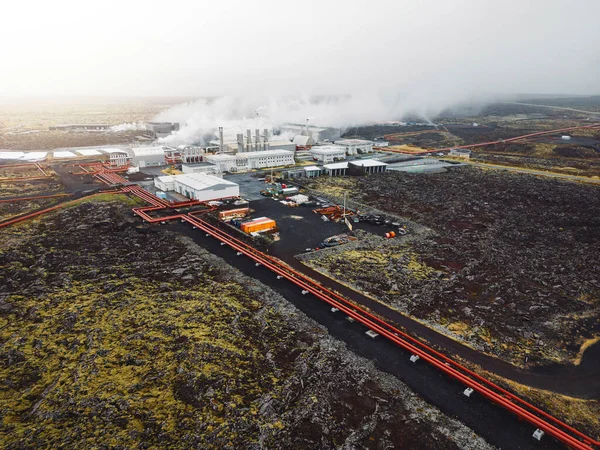 Geothermal Power Plant, hot water power station in Iceland. Steam rolling out of the plant chimneys, red large tubes running across the grounds filled with hot water. Sustainable, energy efficient