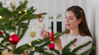 Kafkas kadının Noel ağacını kırmızı süslemelerle süslediği yavaş çekim videosu. Doğal Noel ağacı, kırmızı ve beyaz süsler. Tatiller, şenlik zamanı. Noel ışıkları. 