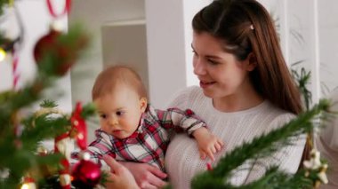 Beyaz giysiler içinde Noel ağacına bakan üç kişilik beyaz bir aile. Kırmızı bir elbise giyen bir bebek. Noel gününde sevgi dolu bir aile..