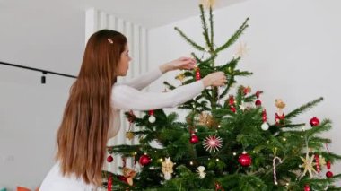 Kafkas kadının Noel ağacını kırmızı süslemelerle süslediği yavaş çekim videosu. Doğal Noel ağacı, kırmızı ve beyaz süsler. Tatiller, şenlik zamanı. Noel ışıkları. 