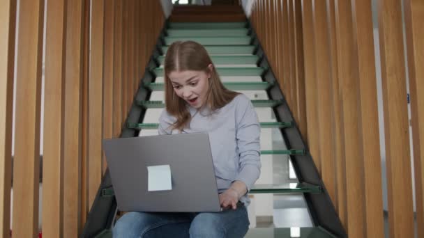 兴奋的年轻的高加索女人坐在楼梯上 膝盖上架着笔记本电脑 观看比赛 为她最喜爱的球队欢呼 — 图库视频影像