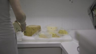 Unrecognizable dairy farm worker view from the back, cutting cheese into selling portions and putting it in plastic bags.