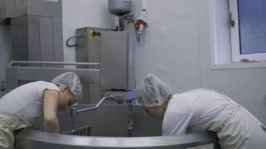 Caucasian women working at the dairy farm on the production line, packaging product, operating with machines mixing the milk, and making cheese curds. Dairy factory worker wearing all white uniform