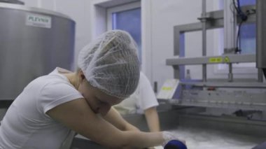 Caucasian women working at the dairy farm on the production line, packaging product, operating with machines mixing the milk, and making cheese curds. Dairy factory worker wearing all white uniform