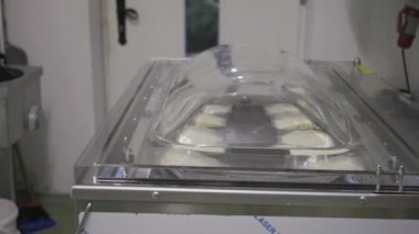 Vacuum machine at the dairy farm sealing the portioned pieces of cheese into plastic bags, the lid opens and unrecognizable worker takes them out. 