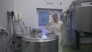 Caucasian women working at the dairy farm on the production line, packaging product, operating with machines mixing the milk, and making cheese curds. Dairy factory worker wearing all white uniform