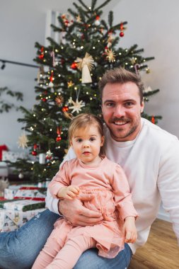 Portrait of young caucasian man with his daughter, decorating the Christmas tree. Loving dad having fun with his little girl on Christmas. 