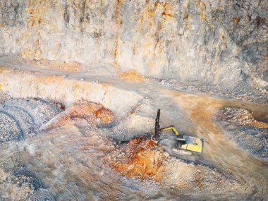 Aerial view of open pit quarry with heavy machinery working on the grounds. Excavators and trucks driving on the grounds. Sunny day in the countryside. 