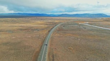 İzlanda dağları, F yolları, nehir geçidi. İzlanda 'da bir yerlerde uzak toprak yol, canlı yeşil çalılar ve volkanik arazilerle çevrili. Çakıl yolunda tek başına giden bir araba.. 