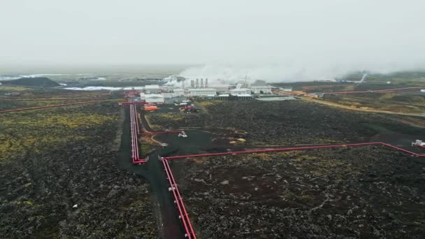 地熱発電所 アイスランドの温水発電所 工場の煙突から蒸気が出て お湯で満たされた地面を走っている赤い大きなチューブ 持続可能でエネルギー効率の高い — ストック動画