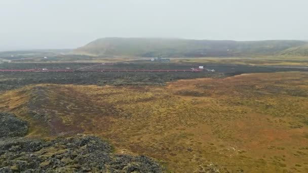 地熱発電所 アイスランドの温水発電所 工場の煙突から蒸気が出て お湯で満たされた地面を走っている赤い大きなチューブ 持続可能でエネルギー効率の高い — ストック動画