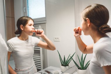 Young caucasian woman getting ready in a bright white modern bathroom. Woman doing her skincare, cleaning her face, teeth and body int he bathroom. 