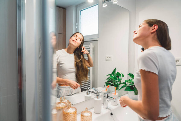 Young caucasian woman getting ready in a bright white modern bathroom. Woman doing her skincare, cleaning her face, teeth and body int he bathroom. 