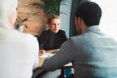 Meeting with clients. Caucasian woman, designer, meeting with her clients, sitting by the desk, consulting on a project. Business meeting. Caucasian people having a meeting in an office. 