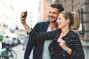 Young millennial couple living in the city, taking a selfie with a smart phone. 