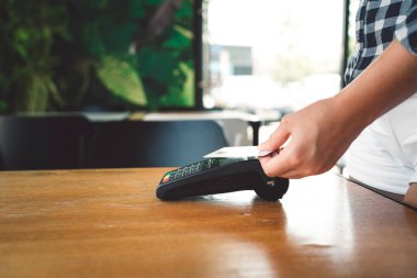 Young caucasian person using a wireless payment method. Young person holding her credit card next to a card reader, paying for her coffee. 