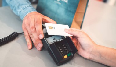 Young caucasian person using a wireless payment method. Young person holding her credit card next to a card reader, close up.