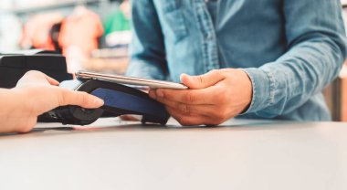 Young caucasian person using a wireless payment method. Young person holding her credit card next to a card reader, paying for her coffee. 
