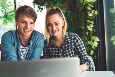 Young caucasian couple of students sitting at a cafe online shopping on their laptop. Both smiling while looking at the laptop. 
