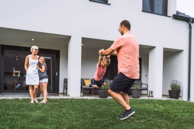 Happy caucasian family of four, mother father and children at home, outdoors playing on the grass, and indoors in the living room having fun as a family. 