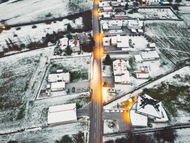 Aerial view of suburban community in winter time in the evening. Snow on the grounds, dark, street lights shining. 