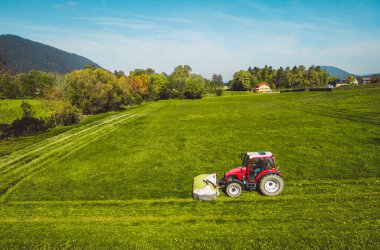 Bir traktörün yeşil taze çimen tarlasını biçtiği hava manzarası, modern bir traktörde bir çiftçinin güneşli bir günde yeşil taze çim biçtiği. Yüksek kalite fotoğraf