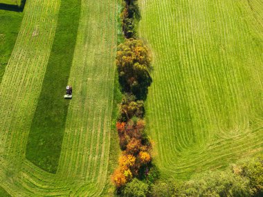 Aerial view of a tractor mowing a green fresh grass field, a farmer in a modern tractor mowing a green fresh grass field on a sunny day. High quality photo