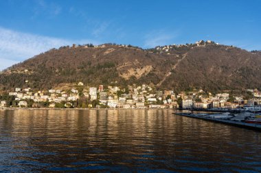 Arka planda büyük bir su kütlesi olan güzel bir şehir manzarası. Su sakin ve uzaktaki binaları ve dağları yansıtıyor. Huzur ve sükunet kavramı