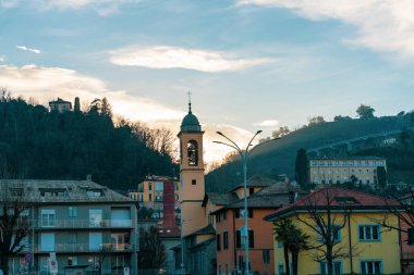Kilisesi ve çan kulesi olan küçük bir kasaba. Gökyüzü bulutlu ve güneş batıyor.