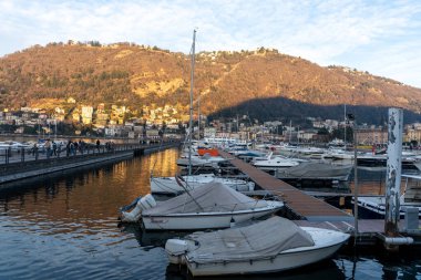 Bir grup tekne marinaya yanaşmış, bazıları muşambayla kaplanmış. Sahne huzurlu ve huzurlu, tekneler güneşin ışınlarını suda yansıtıyor.